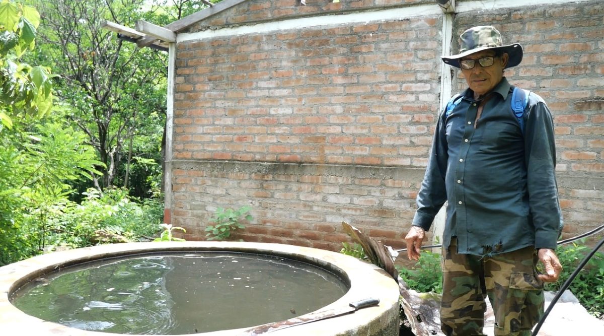 A man stands next to a well full of water.